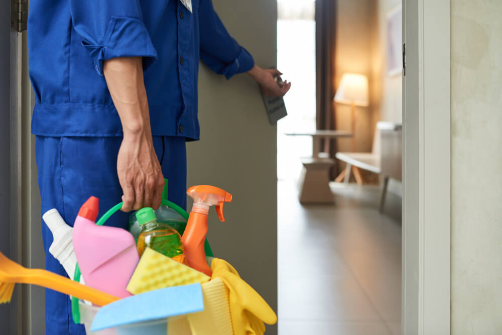 image of a professional cleaner walking into a room while carrying a basket full of cleaning supplies