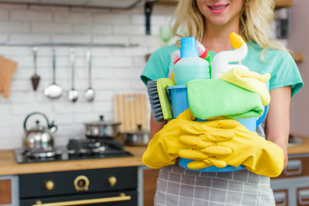 a woman holding some cleaning materials inside a blue basket