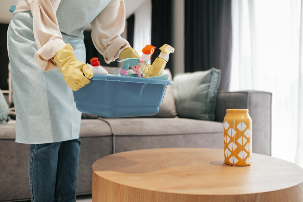 a professional cleaner placing a basin of cleaning tools on the wooden table
